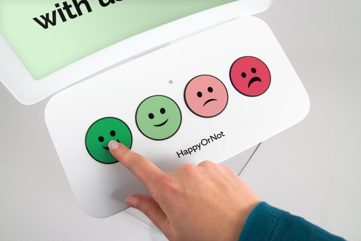 HappyOrNot-smiley-terminal-faces A hand pressing a feedback button.