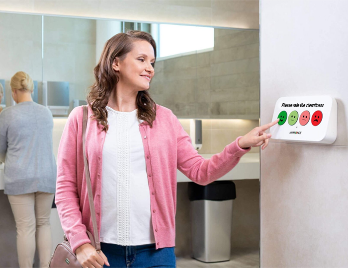 Woman rating restroom cleanliness with HappyOrNot Smiley Terminal wall